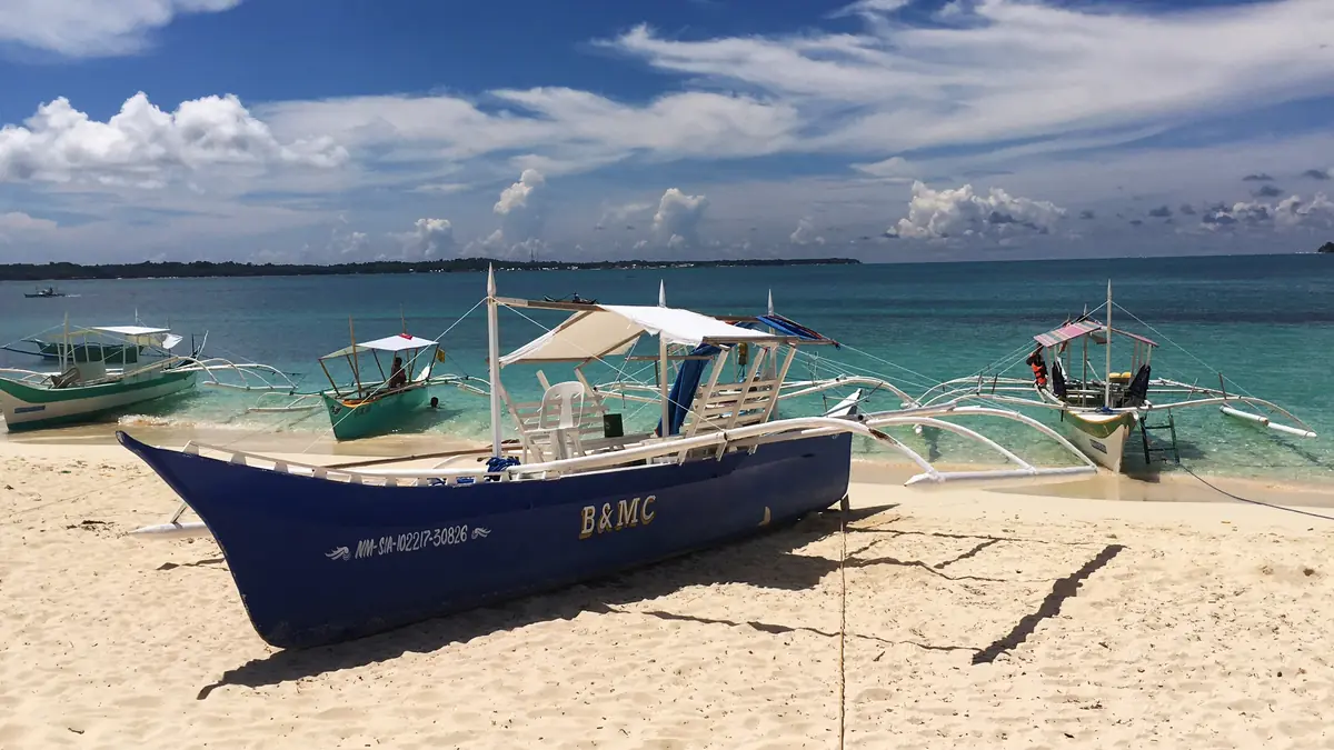 Traditional bangka outrigger boats pulled up on a white-sand beach in Siargao