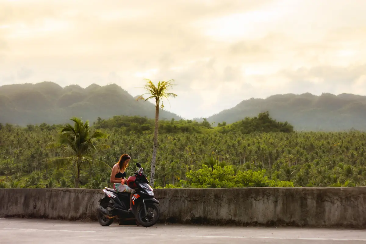 A traveller on a scooter at the Coconut Trees View Deck, with palm groves and hills behind