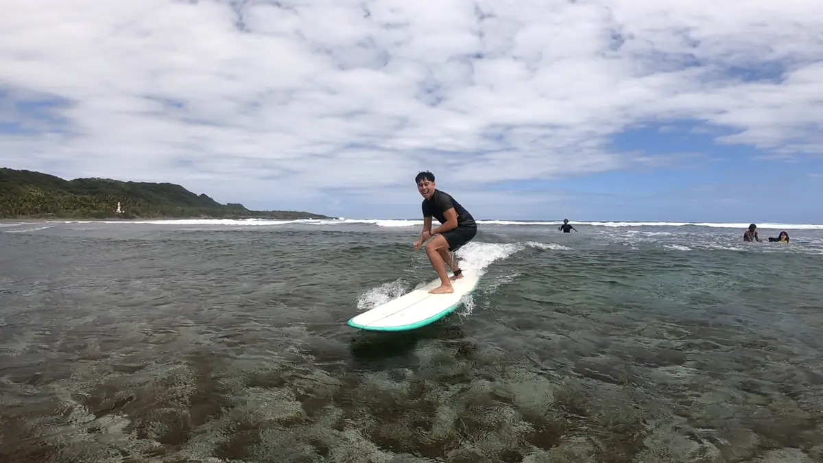 A smiling surfer rides a white longboard across clear, shallow water in Siargao